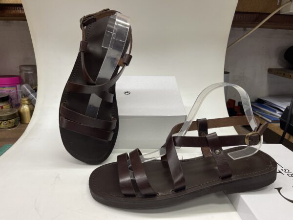 Sandalias de mujer en color marrón oscuro, con diseño de tiras y suela plana, exhibidas sobre un soporte blanco. Perfectas para el verano y ocasiones informales.