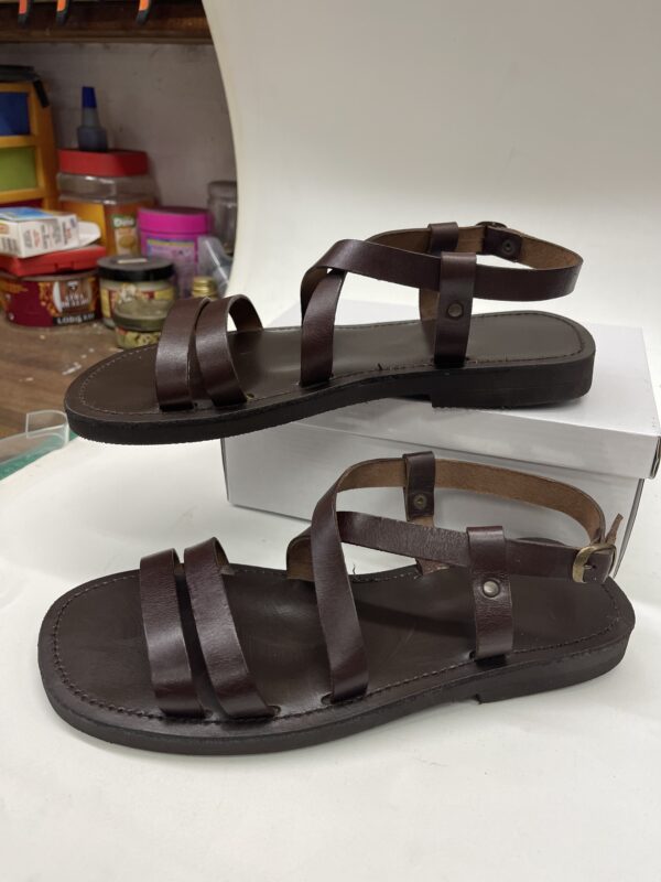 Sandalias de cuero marrón con tiras ajustables, ideales para el verano, mostradas sobre una superficie blanca.