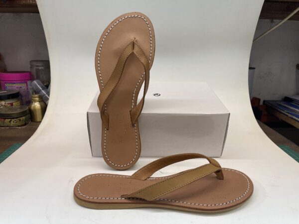Chanclas de mujer de color marrón con tiras delgadas, sobre una superficie blanca y con una caja de fondo. Ideal para uso casual y veraniego.