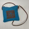 Bolso cruzado azul con diseño de espiral marrón y correa de cuero. Ideal para un look casual y moderno.